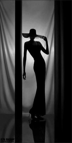 Woman in a wide brim hat and long dress in silhouette against a bright background