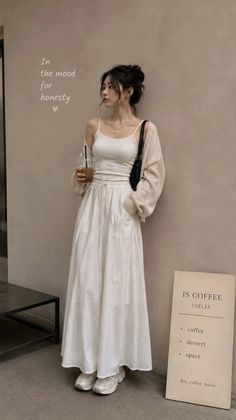 Woman in a white top and long skirt with a cardigan, holding a drink