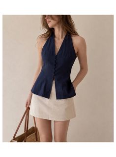Woman in a navy halter top and beige mini skirt holding a straw bag