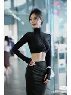Woman in a black crop top and skirt with exposed midriff indoors