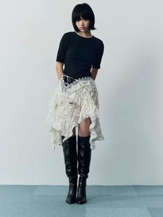 Woman with short black hair wearing a black top and ruffled white skirt