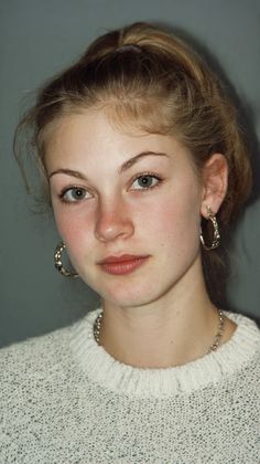 Young woman with blonde hair in a ponytail wearing a white sweater and hoop earrings