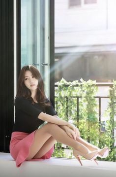Woman with long hair in a pink skirt and high heels sitting outdoors