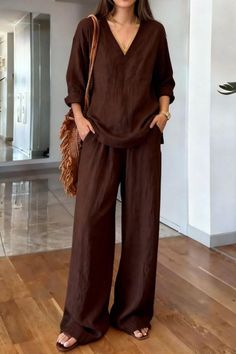 Woman in a brown linen top and wide leg pants with a straw bag indoors