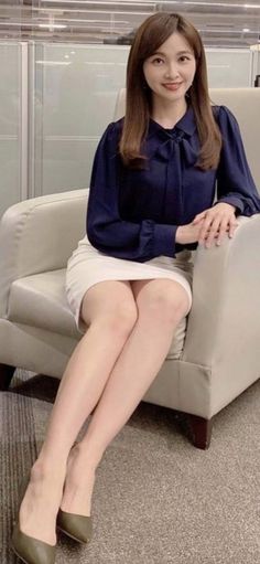 Woman with long hair in a navy blouse and white skirt sitting indoors