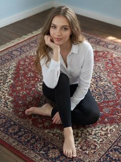 Woman with long hair in a white shirt and black leggings sitting on a patterned rug