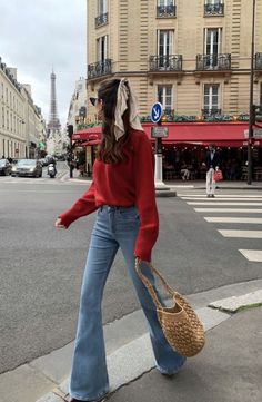 Woman in a red sweater and flare jeans walking on a city street with the Eiffel Tower in the background