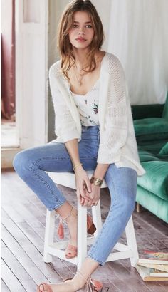 Woman with long hair wearing a white cardigan and blue jeans, sitting indoors