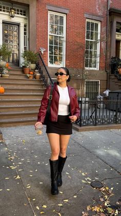 Woman in a red jacket and black mini skirt walking on a street with autumn leaves