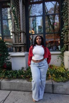 Woman in a red jacket and white crop top with light wash jeans outdoors