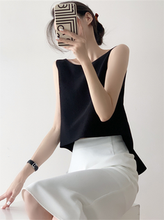 Woman in a black top and white skirt holding a phone to her face