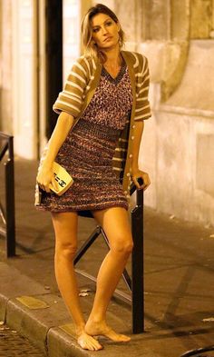 Woman with blonde hair in a short dress and cardigan standing barefoot outdoors at night