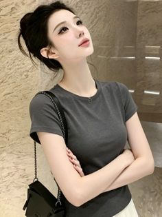 Woman with dark hair in a bun wearing a gray t-shirt and necklace indoors