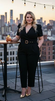 Woman in a black jumpsuit holding a cocktail on a rooftop at golden hour