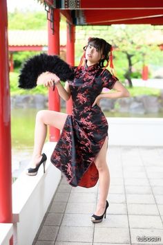 Woman in a black cheongsam with red floral patterns holding a feather fan