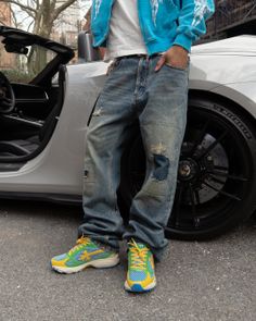 Person in distressed jeans and colorful sneakers leaning against a white sports car