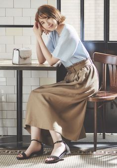 Woman with short hair wearing a pleated top and long skirt sitting at a table