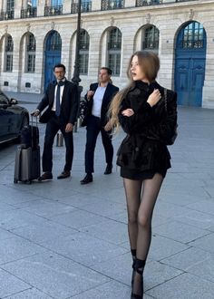 Woman in a black jacket and mini skirt walking on a street with two men