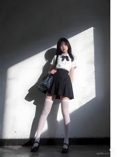 Young woman in a school uniform with dramatic lighting on a white wall