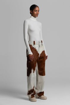 Woman in a white turtleneck and cow print pants in a studio setting