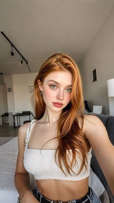 Woman with red hair and green eyes wearing a white crop top indoors