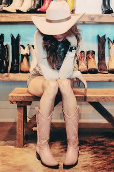 Woman in a cowboy hat and pink cowboy boots sitting on a wooden bench