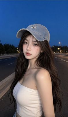 Woman with long hair and a denim cap wearing a white tube top on a street at night