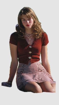 Woman with long hair wearing a red top and gingham skirt, sitting outdoors