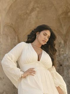 Woman with long dark hair in a white dress with cleavage and jewelry