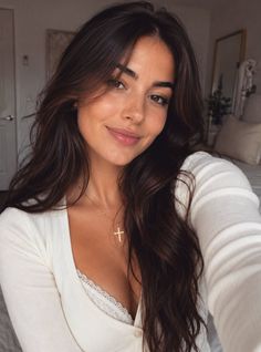 Woman with long brown hair wearing a white top with lace trim and a cross necklace