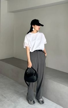 Woman in a white t-shirt and gray pants with a black baseball cap and handbag