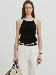 Woman in a black halter top and white pants holding a bag