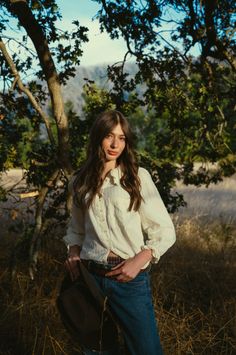 Woman with long hair in a white shirt and jeans in a forest at golden hour