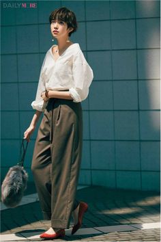 Woman with short hair wearing a white shirt and wide-leg pants, holding a furry bag