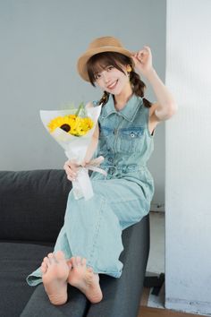 Woman in a denim jumpsuit and straw hat holding sunflowers while sitting on a couch