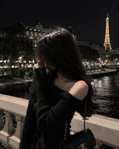 Woman with long dark hair on a bridge at night with the Eiffel Tower in the background