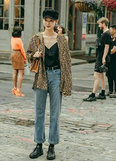 Woman in a leopard print jacket, black cap, and blue jeans on a cobblestone street