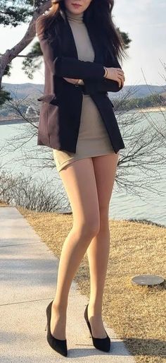 Woman in a black blazer and mini skirt standing outdoors by a body of water