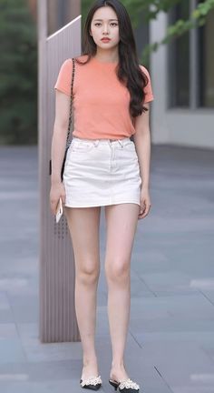 Woman in an orange t-shirt and white mini skirt holding a phone outdoors