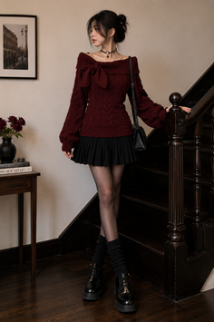 Woman in a maroon off-shoulder sweater and black pleated skirt standing by a staircase