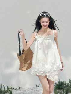 Woman in a white dress and sunglasses holding a straw bag outdoors