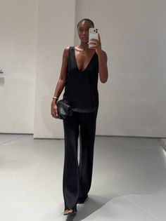 Woman in a black top and wide leg pants taking a mirror selfie