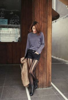 Woman in black shorts and striped tights leaning against a wooden pillar