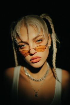 Woman with blonde braided pigtails and orange sunglasses in dramatic lighting