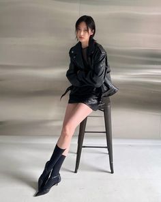 Woman in a black leather jacket and mini skirt sitting on a stool indoors