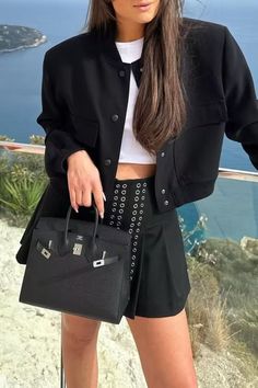 Woman in a black jacket and skirt holding a black handbag outdoors