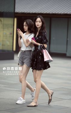 Two women walking on a street, one in a black dress and the other in denim shorts