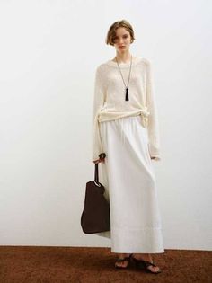 Woman in a white knit sweater and maxi skirt holding a brown bag