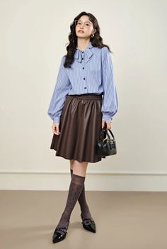 Woman with long hair and glasses wearing a striped shirt and brown skirt