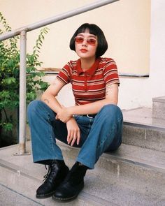 Person with short bob hair and red sunglasses sitting on outdoor steps
